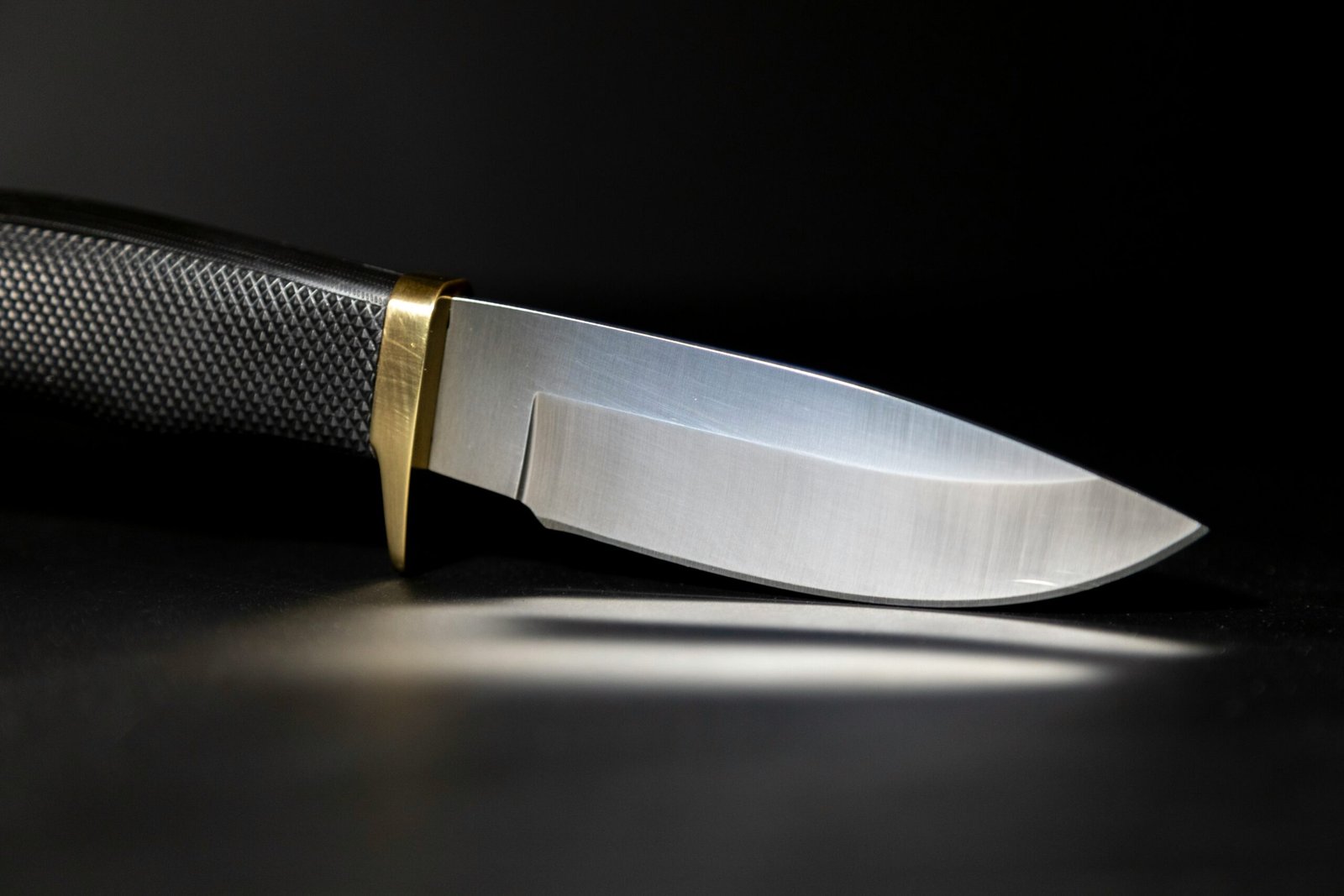 Close-up of a chef’s knife with a textured handle and polished stainless steel blade on a dark surface.